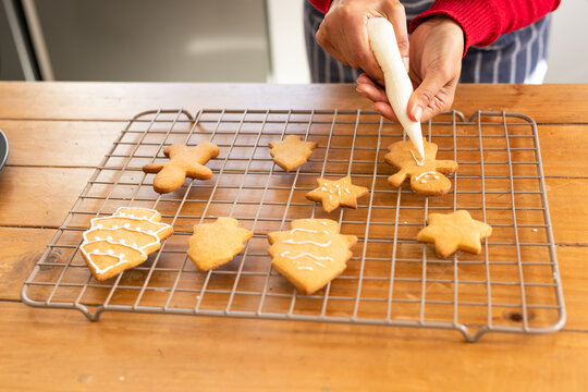 White icing being piped onto gingerbread man cookie on wooden tabletop with assorted iced cookies