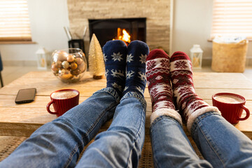 Two pairs of legs resting on coffee table in living room with red mugs ornaments fireplace