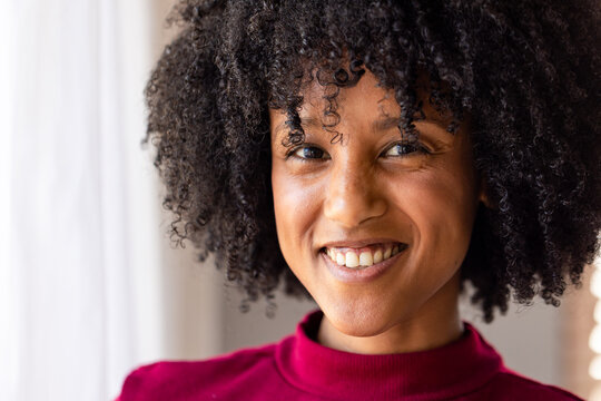 African American woman smiling while standing near window at home wearing red turtleneck sweater