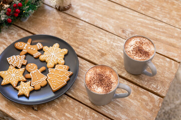 Round plate holding gingerbread cookies with frothy cocoa mugs and evergreen sprig on table