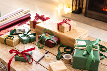 Wrapped gifts resting on wooden tabletop near glowing fireplace, with ribbons, dried orange tags
