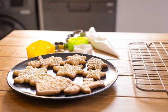 Black round plate holding icing-decorated gingerbread cookies on wooden table near colorful cutters
