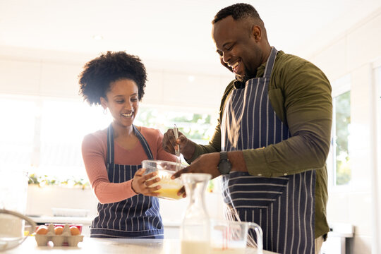 African American couple wearing striped aprons mixing eggs in glass bowl with whisk in kitchen
