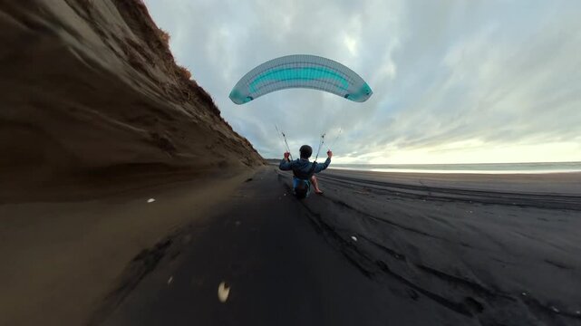Paraglider flying extremely low over the ground at high speed along coastal sand dunes in New Zealand, creating a strong sense of motion and speed