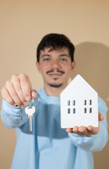 Cheerful blurred man extending his hand showing a key and a wooden house, concept of real estate,...