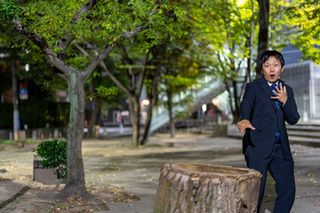 大きな切り株を指さして驚くサラリーマン、夜の公園で思わず驚愕するスーツ男性
