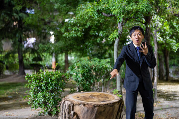 大きな切り株を指さして驚くサラリーマン、夜の公園で思わず驚愕するスーツ男性