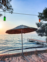 Seaside view with wooden pier and straw umbrella at sunset, peaceful summer evening