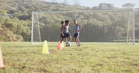 Three boys practicing soccer drills in grassy field, with ball and cones near goal
