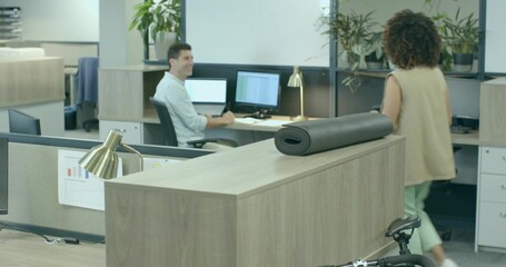 Walking woman wearing beige blazer engaging mature man at open-plan office, bicycle and charts
