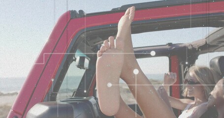 Soaking up sunshine, two friends wearing sunglasses cruising in red open-top SUV by sandy beach