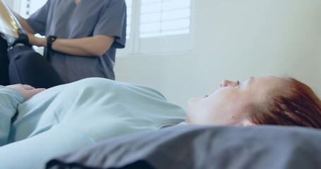 Recording nurse checking patient lying on examination bed in exam room, with tablet and smartwatch