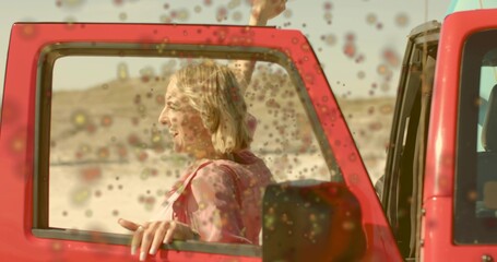 Sitting blonde woman leaning on red vehicle door beside desert road, with floating colored powder