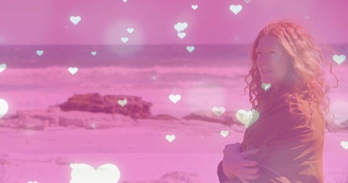 Standing woman wearing shawl at sandy beach with waves, heart overlays, rock outcrop, copy space