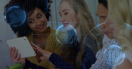 Collaborating four colleagues reviewing tablet on table in office, with holographic globe overlay