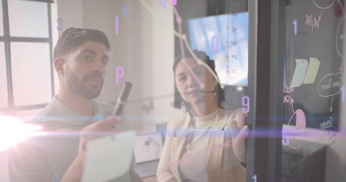 Collaborating duo wearing formal attire analyzing data in meeting room, with glass board