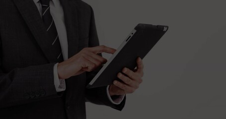 Businessman in dark suit and striped necktie holding tablet computer and tapping screen in studio