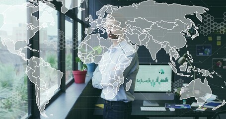 Gazing man wearing light blue shirt by window in office, with computer monitor and potted plants