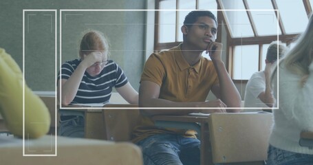 Resting chin, male student in ochre polo shirt gazing right in high school classroom, with desks