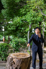 大きな切り株を指さして驚くサラリーマン、夜の公園で思わず驚愕するスーツ男性