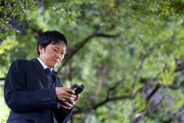 スマートフォンを操作するスーツの男性、夜の公園でスマホを確認するビジネスマン