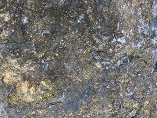 Close-up of a rough stone surface with natural textures, featuring shades of gray, brown, and green moss patches, creating an organic and weathered appearance.