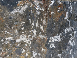 Close-up of a rugged rock surface with natural cracks and textures, featuring shades of gray, white, and golden-brown mineral deposits.