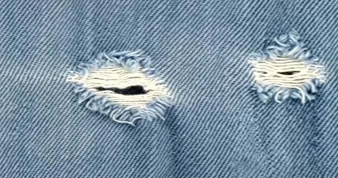 Close-up of distressed blue denim fabric with two small rips, showcasing texture and wear.