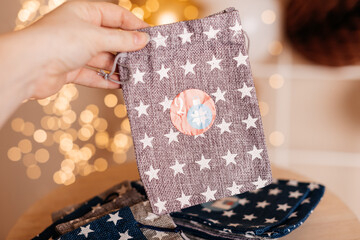 Hand holding a fabric pouch with white stars and number 2 on background of Christmas bokeh