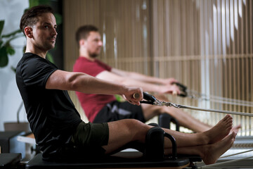 Obraz premium Men engaging in workout routines on reformer pilates machines for strength and flexibility training in a modern fitness studio setting