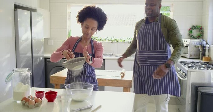 Couple preheating oven, sifting flour, cracking egg and stirring batter on island, copy space
