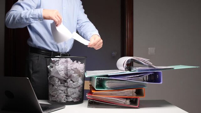 Employee discarding crumpled paper in waste bin feeling frustrated