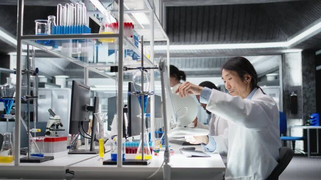Scientist uses laboratory lamp to examine test subject in petri dish. Research facility technician holds medical container to light source, monitoring samples for impurity detection, camera A