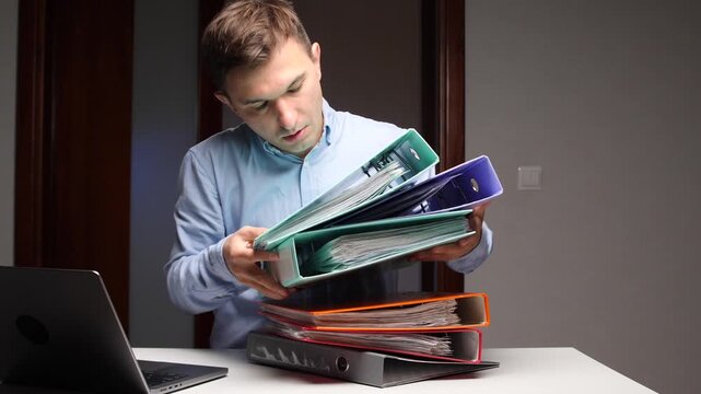 Young man struggling carrying heavy stack of binders