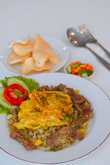 A plate of Indonesian fried rice (nasi goreng) topped with an omelette, served with crackers, pickles, and fresh vegetables on the side. Traditional Asian cuisine captured with bright lighting and app
