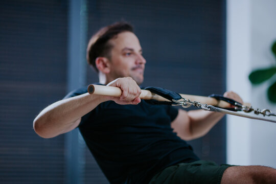 Man performs rowing exercise on reformer pilates machine in modern studio during morning workout session focused on strength and flexibility - Powered by Adobe