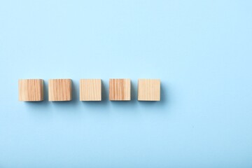 Wooden cubes on light blue background, top view