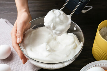 Woman whisking egg whites with hand mixer at black wooden table, closeup