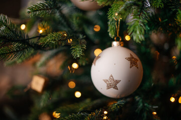 White Christmas ornament with golden stars hanging on decorated tree branch.