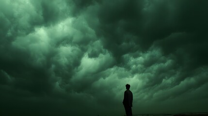 Solitary figure stands beneath an ominous, turbulent mass of dark green storm clouds