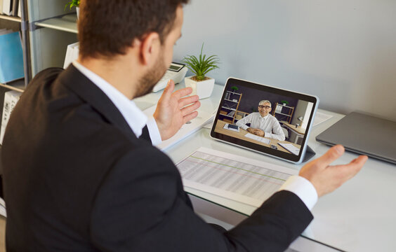 Businessman on tablet during video call. Remote meeting in modern office shows online interview, webinar, clear communication, and expert consulting. Remote teamwork and technology concept.