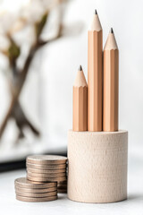 Three wooden pencil wooden cylinder stacked coin minimalist design natural color office accessory small wooden pencils stand with three pencils arranged by height beside stacks of coins