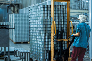 Worker operating a pallet jack to move stacked cans in a food production warehouse Focus on industrial logistics efficiency and organized manufacturing processes.