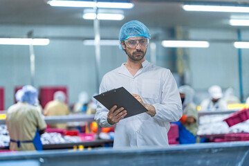 A Quality Assurance (QA) specialist in PPE audits a smart factory floor. He monitors the production area and hygiene compliance for the AI-driven automated system.