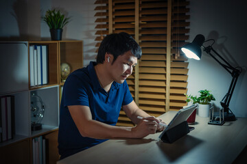 man using tablet and wireless earbuds at night