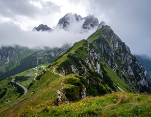 A winding trail and a road snake across the green slopes of a mountainous landscape with cloudy, craggy peaks
