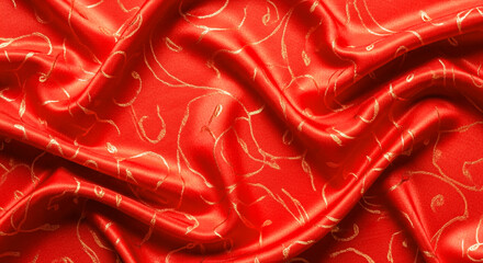 Golden patterns adorn the smooth and vibrant red satin fabric creating luxurious folds and textures