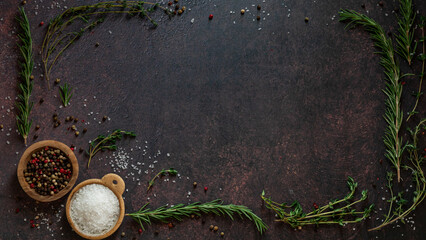 A frame of herbs with salt and peppercorns against a dark background.