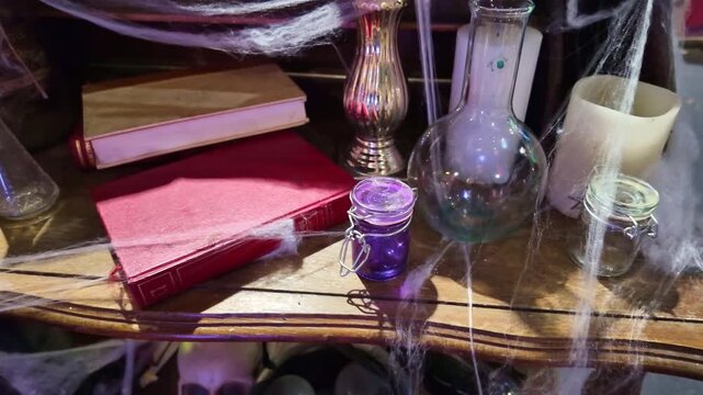 Halloween themed table decorated with cobwebs skulls, candles and potion bottles under direct light.