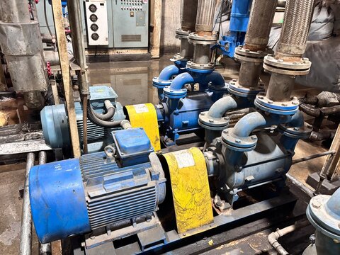 A pair of electric blue industrial centrifugal pumps and motors with associated heavy piping, possibly in a factory basement or pump room, showing a fluid transfer system for water, chemical, or waste